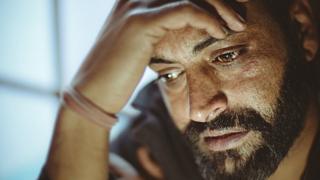 Bearded man holding his head in his hand and tearing up