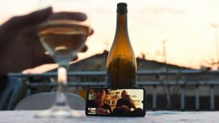 A woman shares a drink with friends via a video call