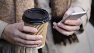 Woman holding coffee while using smartphone