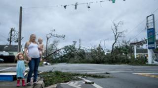 Mujer con sus hijos viendo la destrucción del huracán Michael en una calle
