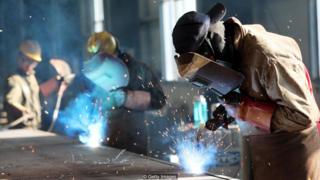 Homens trabalham usando maçaricos em indústria