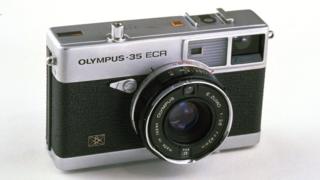 An Olympus-35 ECR rangeinfer-style camera with a short "pancake" lens is seen here against a white background