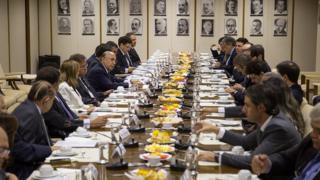 Meirelles comanda reunião ao lado de outras pessoas sentadas em mesa, e com fotos de ex-ministros ao fundo, em foto de 2016