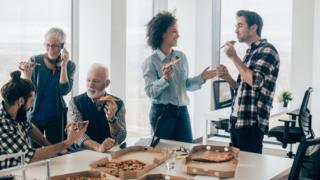 Gente en la oficina comiendo pizza