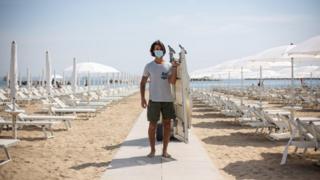 A man wearing a mask laying out deck chairs in Italy