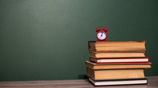 Reloj diminuto sobre libros y tablero