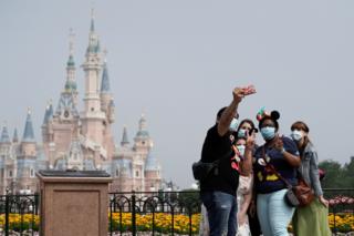 Visitors wearing protective face masks pose for a picture at Shanghai Disney Resort