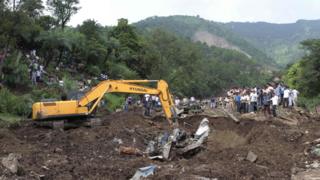 Heavy machinery removes debris as rescue personnel search for survivors and bodies of victims after a landslide along a highway at Kotrupi