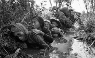 Women and children crouch in a muddy canal as they take cover from intense Viet Cong fire at Bao Trai, about 20 miles west of Saigon, Vietnam, on 1 January 1966.