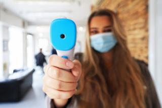 A staff member holds up a thermometer to the camera in a hairdressers
