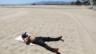 Man sunbathing in a mask on a closed and empty beach in Santa Monica, California