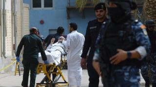 Kuwaiti emergency personnel pull a man on stretchers past security forces outside the Shiite Al-Imam al-Sadeq mosque after it was targeted by a suicide bombing during Friday prayers on June 26, 2015, in Kuwait City. T