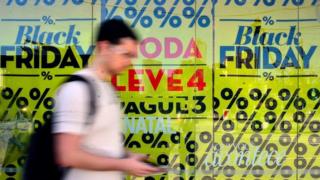 Homem passa em frente à vitrine com cartazes da Black Friday