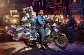 A man posed on his motorcycle with lots of large water containers stacked on top of each other