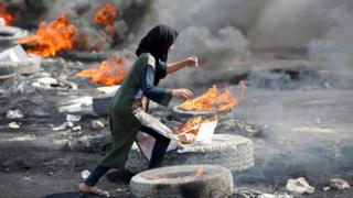 A protester runs between burning tyres in Baghdad, Iraq (3 October 2019)