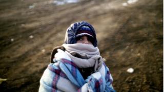 Ребенок-мигрант, завернутый в одеяло, пытается согреться возле македонско-сербской границы