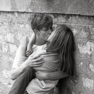 A couple kiss as they lean against a wall