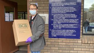 Man wearing mask holding box of hand sanitiser outside Cardiff prison