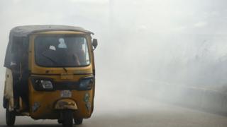 A rickshaw carries passengers through smoke emitted from a dump in the city of Port Harcourt