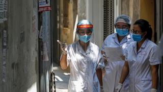 Healthcare workers are seen at a lane near the house of a COVID-19 patient as they investigate infection links in Hanoi