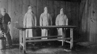 Tres hombres con batas y máscaras protectoras en el hospital de tratamiento de la peste en China, en 1910-11