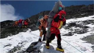Sherpa with climber strapped to his back
