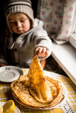 A child picks up a pancake off a plate