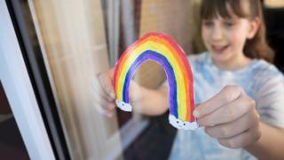 Girl sticks rainbow drawing on window at home