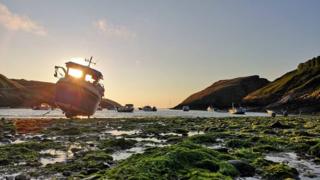 Sun sets behind boat as viewer looks out to sea