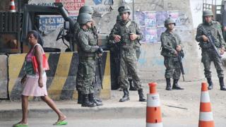 Mulher passa por militares na Maré, em 2014