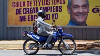 People pass an election campaign poster of presidential candidate Gonzalo Castillo in Santo Domingo, Dominican Republic, 05 June 2020.