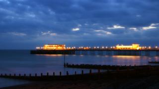 The illuminated pier glows against a cloudy evening sky