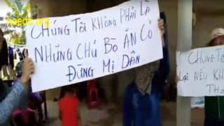 Người biểu tình giơ cao biểu ngữ trước cửa nhà trưởng thôn Cồn Sẻ