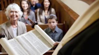 люди в синагоге смотрят, как читают свиток Торы
