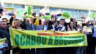 Abashingamateka bo mu migambwe itavuga rumwe na leta bafashe icapa kivuga ngo " N'abagasaga Muvema, isoko ryarakamye" mu myiyerekano yo kuwa 12/04/2016 yabera Brasilia