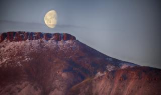 A large full moon above a reddish landscape
