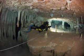 Xisco Gracia swimming through a cave. His torch lights up a guideline