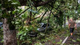 A man walks near a car hit by a falling tree following a storm in Timisoara, western Romania. Photo: 17 September 2017