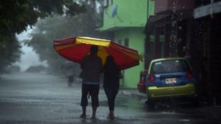 Dos personas caminando bajo una fuerte lluvia en Tecolutla, Veracruz, México.