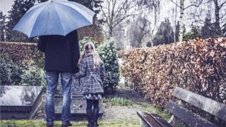 Hombre con niña frente a una tumba