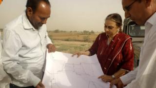 Amla Ruia with two engineers looking at plans outside in dry terrain