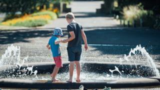 Dos niños juegan en una fuente en los jardines.