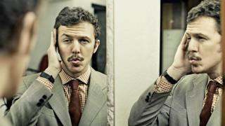 Man looking adoringly at his own reflection in a mirror.