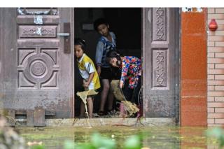 Children remove water from inside their house in Longkou village due to torrential rains in Poyang county, Shangrao city, in China's central Jiangxi province on 16 July 2020