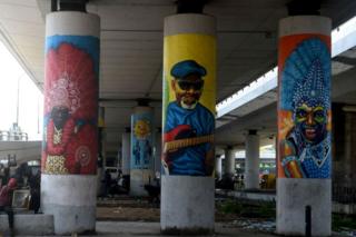 People sit and stand by pillars with street art portraits 22 July 2019.