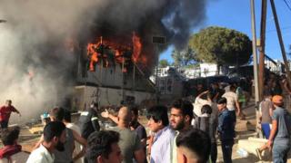 People stand near a burning container at the Moria refugee camp, Lesbos, Greece. Photo: 29 September 2019