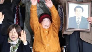 Kim Seong-ju (tengah) di antara para korban dan keluarga yang merayakan kemenangan mereka di Seoul.