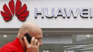 Man walks in front of a Huawei sign