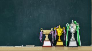 Três troféus em frente a lousa