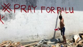 Мужчина пишет слова «Молись за Палу» на стене в Палу